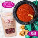 A bowl of red salsa with tortilla chips sits beside a Rico Rico Dried Mexican Chiles 3-Pack—including ancho, guajillo, and arbol peppers—and a green cloth napkin. Text in pink boxes reads Authentic Mexican Flavor and RICO! RICO! Pair these gourmet chiles from Rico Rico with your favorite spice kit for an unforgettable taste experience.
