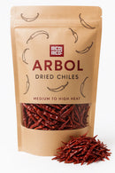 A brown bag labeled "Rico Rico Chile de Árbol Dried Chiles – Hot & Authentic Mexican Peppers" featuring vibrant red peppers inside and a small pile of dried chiles in front, ideal for adding genuine Mexican flavor to your favorite dishes.