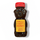 A bear-shaped plastic bottle with a red cap, labeled Guenther Apiary Arkansas Hot Honey Bear. The yellow label features red text and flame icons, emphasizing this bold and flavorful spicy honey blend made from wildflower honey.