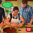 A woman in an apron teaches two people to cook authentic Mexican cuisine, showing them how to wrap ingredients in green leaves. On the table sits a bowl of flavorful filling, seasoned with Rico Rico Arbol Chile Powder Shaker. “Authentic Mexican Flavor” and “Rico! Rico!” appear in the image corners.