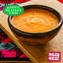 A rustic bowl of orange salsa sits on a wooden board with colorful fabric underneath, its authentic Mexican flavor and bold heat brought to life by Rico Rico Habanero Chile Powder Shaker. A green label reads Authentic Mexican Flavor, while a red Rico Rico logo appears in the corner.