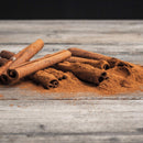The Spice Lab Cinnamon Powder 12 oz is artfully displayed on a rustic wooden surface with a dark background, emphasizing the rich color and enchanting aroma of this high-oil cinnamon variety by The Spice Lab.