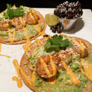 Two seafood tacos on crispy tostadas topped with guacamole, grilled shrimp, cheese, cilantro, and a drizzle of Terrapin Ridge Farms Chile Lime Aioli Squeeze Garnishing Sauce are served with black beans and a lime wedge.
