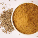 A bowl of The Spice Lab Organic Ground Cumin sits next to a small pile of whole cumin seeds on a light surface—an ideal choice for enhancing curry recipes or adding depth of flavor to BBQ rubs.