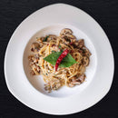 A plate of spaghetti topped with minced meat, mushrooms, two red chili peppers, and The Spice Lab Savory Whole Leaf basil is served on a white plate against a black background.