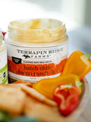 An open jar of Terrapin Ridge Farms Hatch Chile Bacon Ranch Dip sits on a plate with sliced yellow and red bell peppers and crackers. This creamy southwest dip by Terrapin Ridge Farms offers a rich, smoky flavor in every bite.