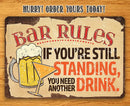 Bar Rules - Metal Sign by Lone Star Art: “If you’re still standing, you need another drink.” Features a beer mug and cocktail glass. Perfect for any bar—order yours today!.