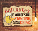 The Bar Rules - Metal Sign by Lone Star Art features a beer mug, cocktail glass, and hanging bulb—reading “If you’re still standing, you need another drink.” Perfect funny bar decor for any wall.