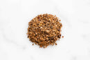 A small pile of World Spice Bar-H Beef Rub by World Spice, featuring coarse, mixed seasoning with visible black, brown, and tan particles, sits on a white surface.