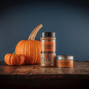 Two pumpkins sit on a wooden surface next to Bourbon Barrel Foods Bourbon Smoked Pumpkin Spice by Bourbon Barrel Foods—one tall shaker and one small tin—set against a dark blue background, highlighting this unique fall-inspired smoky spice blend.
