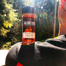 A 3 oz bottle of BBQ Bros Rubs Kansas City Style BBQ Rub by BBQ Bros Rubs, celebrated for its sweet and smoky barbecue flavor, sits on a person’s shoulder outdoors as sunlight filters through the trees in the background.