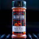 A bottle of BBQ Bros Rubs Texas Style BBQ Rub 5 oz from BBQ Bros Rubs sits on a grill, featuring flames on the label and text reading Authentic Regional Recipes and Net Wt. 5 oz. This brisket seasoning captures the bold flavors of authentic Texas barbecue, making it perfect for your next cookout.