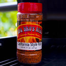A container from the BBQ Bros Rubs Western Style BBQ Rub Gift Set (Large 3-Pack) by BBQ Bros Rubs is placed on a grill, showcasing its red lid and flame-adorned label with bold text—ideal for fans of regional BBQ flavors and authentic Western-style rubs.