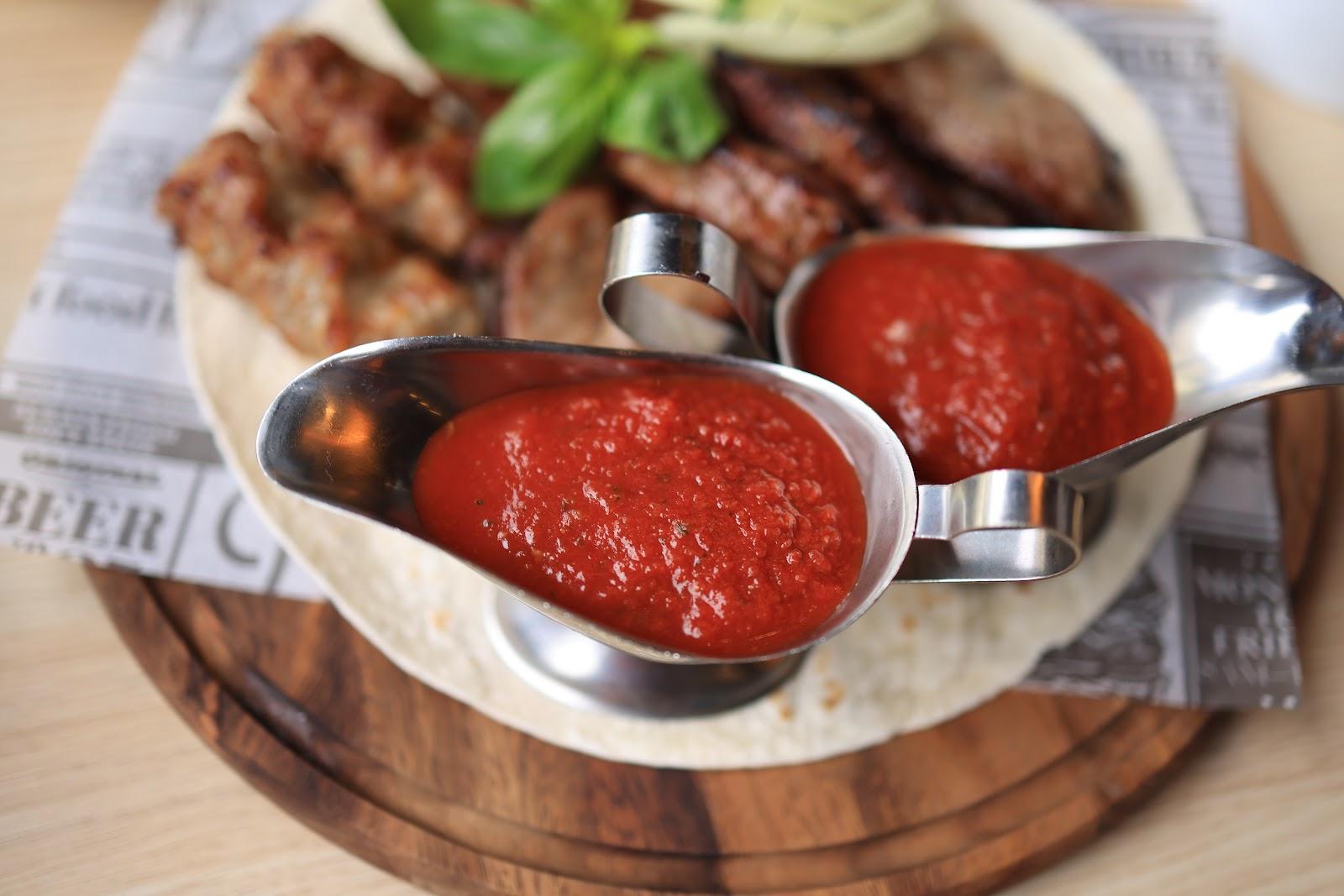 Two metal sauce boats of red BBQ sauce served with grilled meats