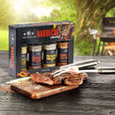 The Spice Lab Barbecue Seasoning Collection by The Spice Lab, featuring four spice jars, is displayed next to grilled steak on a cutting board, grill tools, and an outdoor grill in a sunlit green backyard. This flavorful barbecue rub and seasoning set makes the perfect grilling gift for any outdoor cooking enthusiast.