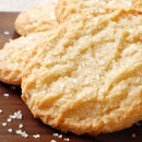 Close-up of sugar cookies topped with The Spice Lab’s Sanding Con AA Sugar, resting on a wooden surface. A few loose crystals of this decorative sugar are scattered around the cookies—perfect for enhancing your baked creations.