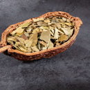 A cracked-open pod filled with dried green leaves, like The Spice Lab Cracked Bay Leaves 1 lb Bulk Foodservice Herb, sits on a dark gray textured surface.