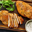 Two seasoned chicken breasts rest on a wooden board, one whole and one sliced, accompanied by fresh arugula and a small bowl of creamy dipping sauce. The chicken is enhanced with The Spice Lab Flavors of Provence Seasoning Set by The Spice Lab, bringing gourmet French and Italian-inspired flavor to every bite.