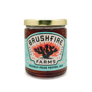 A jar of Brushfire Farms Prickly Pear Pepper Jam featuring a gold lid and a vibrant label adorned with a cactus illustration on a white background. This sweet and spicy jam from Brushfire Farms combines the distinctive taste of prickly pear with the bold heat of Chile Pequin pepper, creating an unforgettable flavor experience.