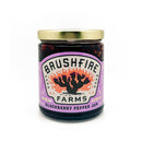 A jar of Brushfire Farms Blackberry Pepper Jam, topped with a gold lid and adorned with a purple label featuring a cactus illustration and branding, delivers sweet heat that elevates wild game dishes or your favorite snacks.