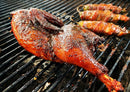 A seasoned, smoked whole bird and bacon-wrapped jalapeños cook on a grill with visible grill marks and smoky flavor, the food glistening with spices and juices, while a sweet heat from Brushfire Farms’ Brushfire Glaze brings extra sparkle to every bite.