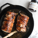 Two browned pork tenderloins in a cast iron skillet with a glaze, a basting brush on the skillet, and a jar of Terrapin Ridge Blueberry Bourbon Pecan Jam 5 oz by Terrapin Ridge Farms—ideal for charcuterie boards or as unique hostess gifts.