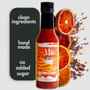 A bottle of Culture Hot Sauce Blindsided by Culture Hot Sauce sits beside text reading clean ingredients, hand made, no added sugar, with sliced blood oranges and chili flakes in the background—an irresistible smoky citrus hot sauce created for bold flavor lovers.