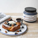 A plate of thick French toast with whipped cream, blueberries, pecans, and powdered sugar is served beside a metal cup of gourmet jam. In the background is a jar of Terrapin Ridge Farms Blueberry Bourbon Pecan Jam Quart.