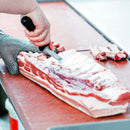 A skilled cook expertly slices meat on a cutting board using the sharp chef's knife from the SpitJack Barbecue Knife Bundle with Brisket Set.