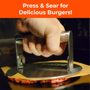 A hand presses the Braize Smash Burger Press with Folding Handle & 50 Non-Stick Paper Sheets onto ground beef on a griddle. White text on orange reads, "Press & Sear for Crispy-Edged Burgers!" Brand: Braize.