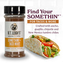 A jar of B.T. Leigh’s Gluten-Free Taco Seasoning sits next to a chicken taco on a soft tortilla, with text describing the blend of ancho, guajillo, chipotle, and New Mexico lumbre chiles.