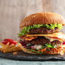 A double cheeseburger with lettuce, cheese, bacon, and sauce in a sesame bun is seasoned with SALTOPIA Smoky Blended Salt: BURGER BUDDY and served with French fries and ketchup on a slate board.