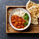 A bowl of chicken curry made with The Spice Lab Organic Indian Curry Powder sits alongside white rice, garnished with fresh cilantro and served with naan bread on a wooden tray.