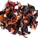 A wooden spoon holds The Spice Lab Whole Hibiscus Flowers—whole dried hibiscus petals from The Spice Lab—while additional petals are scattered on a white background, highlighting this vibrant botanical ingredient perfect for foodservice use.