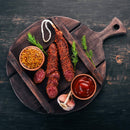 Sliced sausage on a round wooden board with mustard, ketchup, garlic, and fresh herbs, served on a dark rustic background—seasoned perfectly with BBQ rubs and The Spice Lab Organic Smoked Paprika for a rich smoky-sweet flavor.