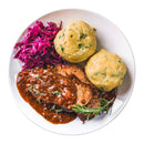 A plate with two bread dumplings and braised beef in brown gravy garnished with rosemary and a hint of The Spice Lab Fancy Chervil, accompanied by red cabbage slaw, all on a white background.