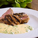 Grilled steak slices on a white plate, served with a creamy fines herbs sauce featuring The Spice Lab Fancy Chervil, inspired by classic French cooking. Green leafy garnish is visible in the background.