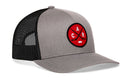 Introducing the Haka Hat Carolina Hockey Trucker Hat | Red CAR X Snapback—a gray and black cap by Haka Hat featuring a bold red circular patch with two crossed hockey sticks, a puck, and the letters C A R. This signature 5.0 trucker is the perfect blend of style and comfort for Raleigh hockey fans looking to show off their team pride.