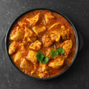A black bowl filled with chicken curry, infused with The Spice Lab Organic Indian Curry Powder and garnished with fresh cilantro, placed on a dark textured surface.