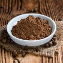 A bowl filled with The Spice Lab Organic Ground Allspice sits on burlap, surrounded by whole allspice berries atop a rustic wooden surface—an essential spice from The Spice Lab for homemade BBQ sauce or classic Jamaican jerk seasoning.