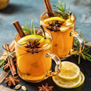 Two glass mugs of hot apple cider are garnished with lemon slices, cinnamon sticks, star anise, and rosemary, featuring The Spice Lab Mulling Spice by The Spice Lab. Slices of lemon and whole mulling spice from The Spice Lab are artfully arranged on a dark surface nearby.