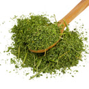A wooden spoon rests on a pile of The Spice Lab Parsley by The Spice Lab, a classic pantry herb widely used in Middle Eastern cooking, with some pieces scattered around on a white background.