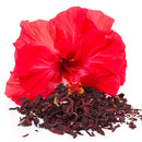 A vibrant red hibiscus flower, a prized botanical ingredient, is displayed behind a pile of The Spice Lab Whole Hibiscus Flowers on a white background.