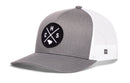 The Haka Hat Charleston Trucker Hat | CHS X Snapback features a gray and white design with a black circular patch displaying crossed lines, the letters C, H, S, and a small state outline. The back is made of white mesh for breathability.