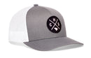 Introducing the Haka Hat Charleston Trucker Hat | CHS X Snapback by Haka Hat—a gray and white trucker hat featuring a black circular patch on the front, showcasing the letters “C H S” and a small state outline separated by crossed lines.