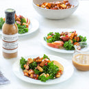 Three white plates with kale salad, apple slices, and roasted veggies highlight sweet and tangy flavors. Terrapin Ridge Farms' Apple Cider Maple Balsamic Vinaigrette sits beside a large salad bowl in the background.