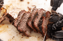 A person wearing black gloves slices juicy, tender smoked brisket with a dark, seasoned crust made using The Spice Guy Colorado Box from The Spice Guy, on a white cutting board.