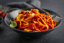 The Spice Guy Colorado Box by The Spice Guy is shown with a black bowl of wide noodles in chunky red tomato sauce, garnished with basil. Perfect for outdoor cooking; a fork rests inside and a dark napkin is seen in the background.