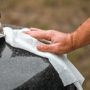 A person is cleaning a black and gray granite surface with Crocodile Cloth® Grill Wipes (80 Count) from Crocodile Cloth, heavy-duty wipes designed for BBQ and grill surfaces often used with outdoor cooking equipment.