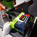 A person grills chicken outdoors, holding a brush and tongs near a barbecue. On the table is Crocodile Cloth® Grill Wipes (80 Count) Heavy-Duty BBQ & Grill Cleaning Wipes by Crocodile Cloth for easy grill cleanup.